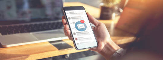 Eine Hand hält ein Handy mit einem Postfach voller E-Mails