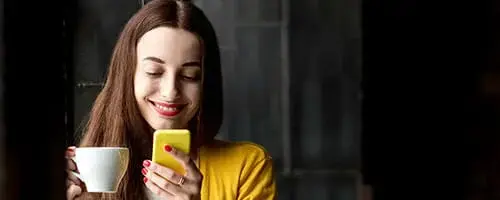 Eine Käuferin blickt glücklich in ihr Handy mit einer Tasse Tee in der Hand