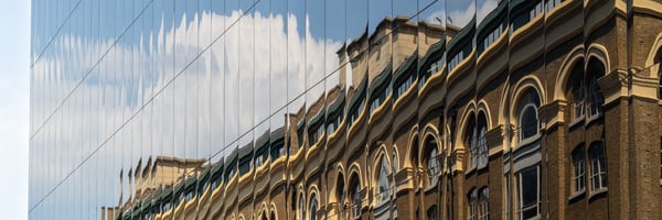 Ein kleineres Gebäude spiegelt sich in der Fassade eines größeren Gebäudes